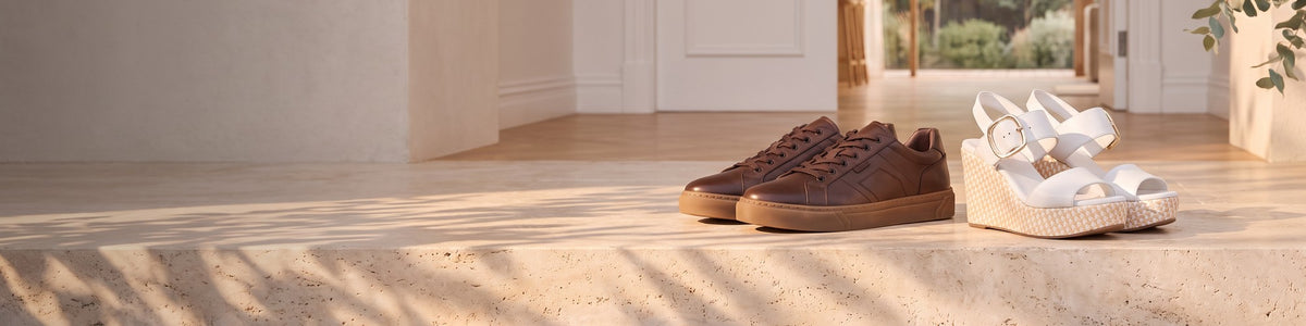 Brown leather sneakers and white wedge sandals on a sunlit floor at home